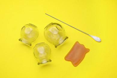 Glass cups, gua sha and torch on yellow background, flat lay. Cupping therapy