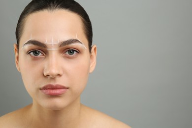 Photo of Eyebrow correction. Young woman with markings on face against grey background, space for text