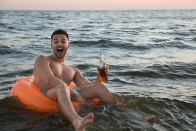 Photo of Happy young man with drink on inflatable ring in water