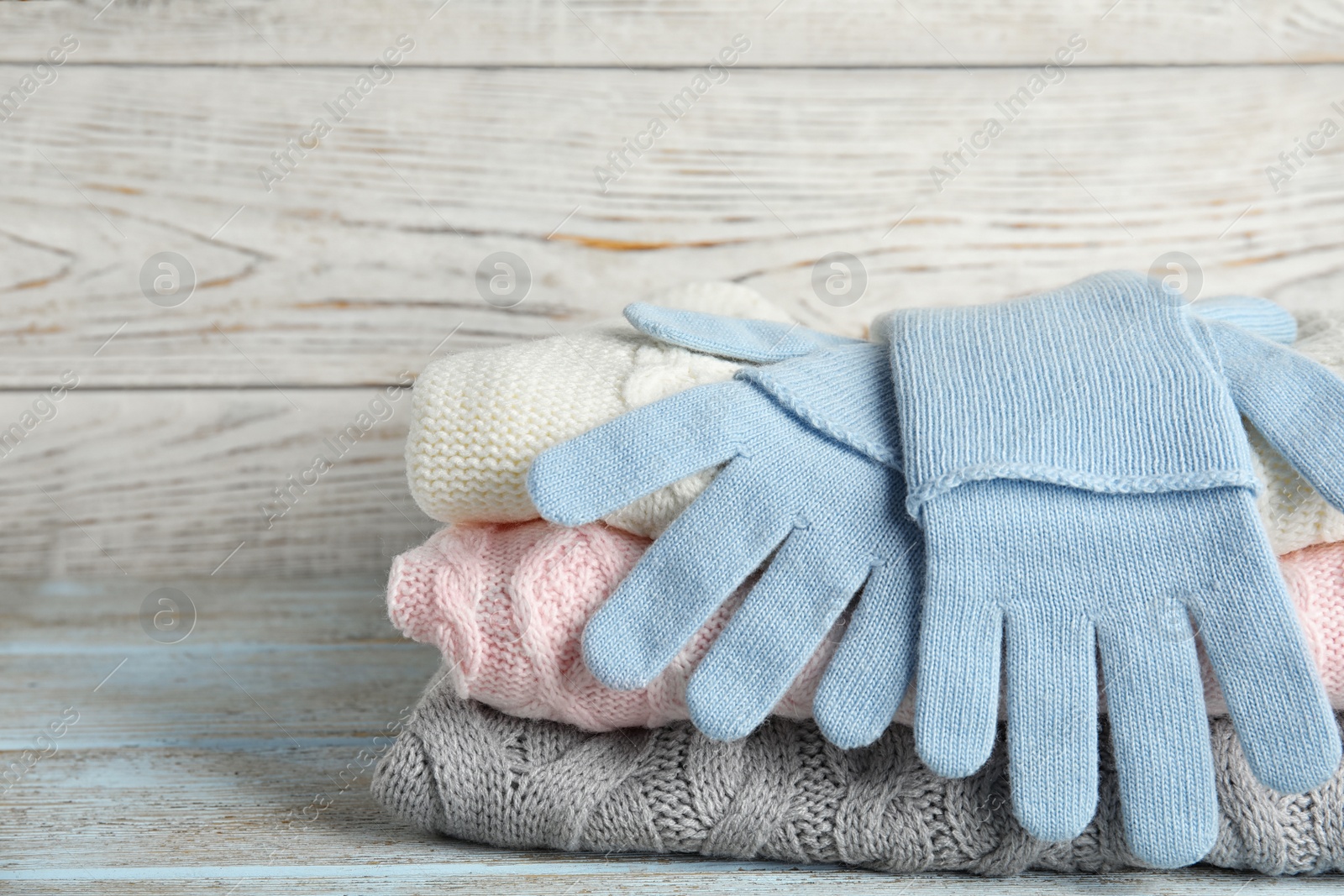 Photo of Stacked sweaters and gloves on wooden table, closeup. Autumn clothes