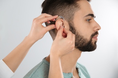 Photo of Otolaryngologist putting hearing aid in man's ear on white background