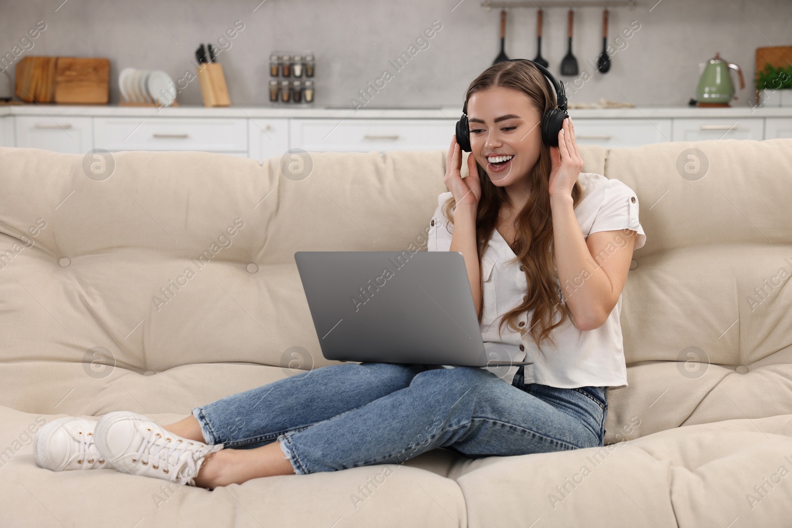 Photo of Happy woman with laptop listening to music in headphones on couch