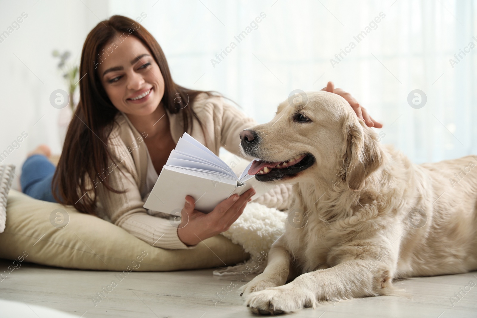 Photo of Young woman with book and her Golden Retriever at home. Adorable pet