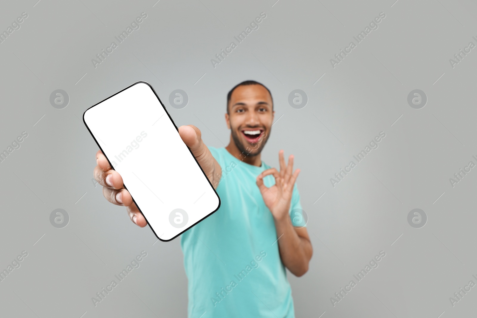 Photo of Young man showing smartphone in hand and OK gesture on light grey background, selective focus. Mockup for design