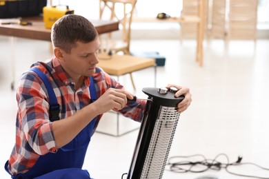 Professional technician repairing electric halogen heater with screwdriver indoors