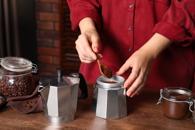 Photo of Woman putting ground coffee into moka pot at wooden table, closeup