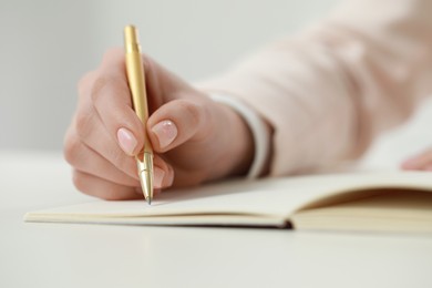 Woman writing in notebook at white table, closeup