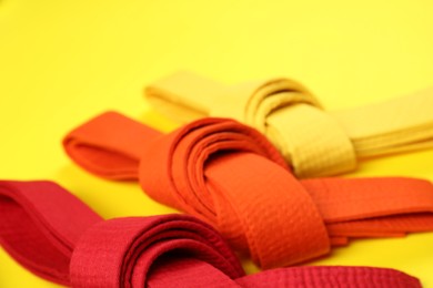 Photo of Colorful karate belts on yellow background, closeup