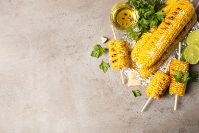 Delicious grilled corn cobs on grey table, flat lay. Space for text