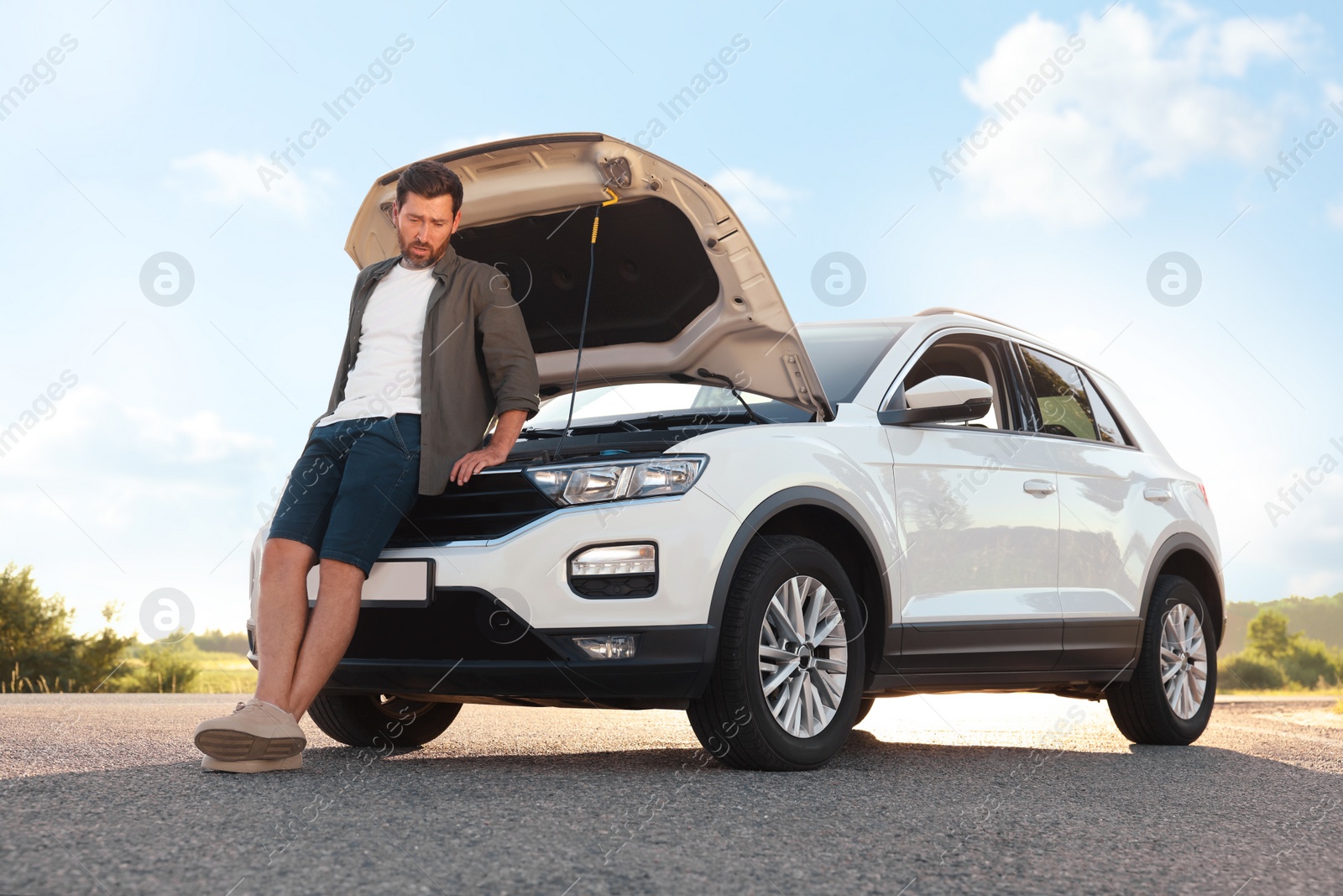 Photo of Upset man near broken car on roadside, low angle view