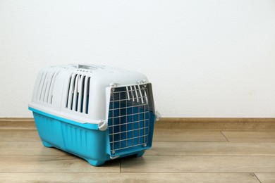 Photo of Light blue pet carrier on floor near white wall. Space for text