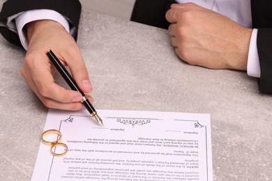 Photo of Man signing marriage contract at light grey table, closeup