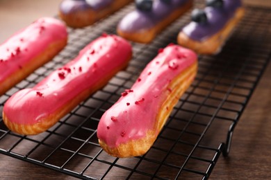 Photo of Cooling rack with different tasty glazed eclairs on wooden table, closeup