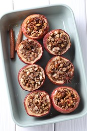 Tasty baked apples with nuts, honey and spices in dish on white wooden table, top view