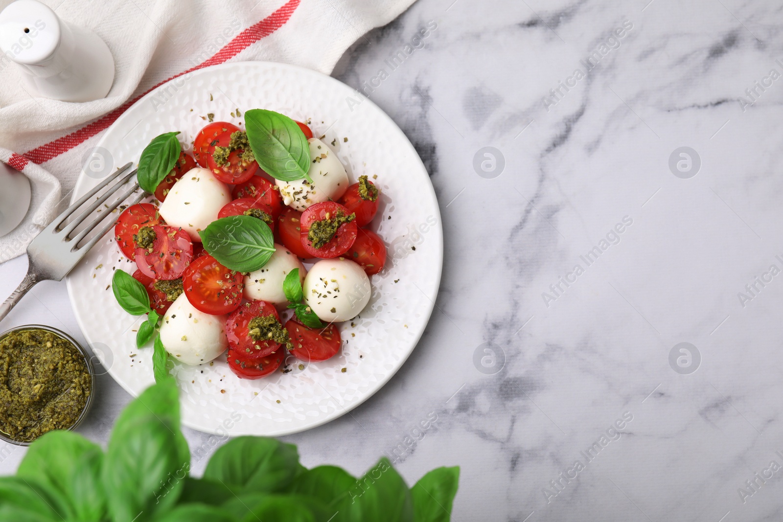 Photo of Tasty salad Caprese with tomatoes, mozzarella balls and basil served on white marble table, flat lay. Space for text