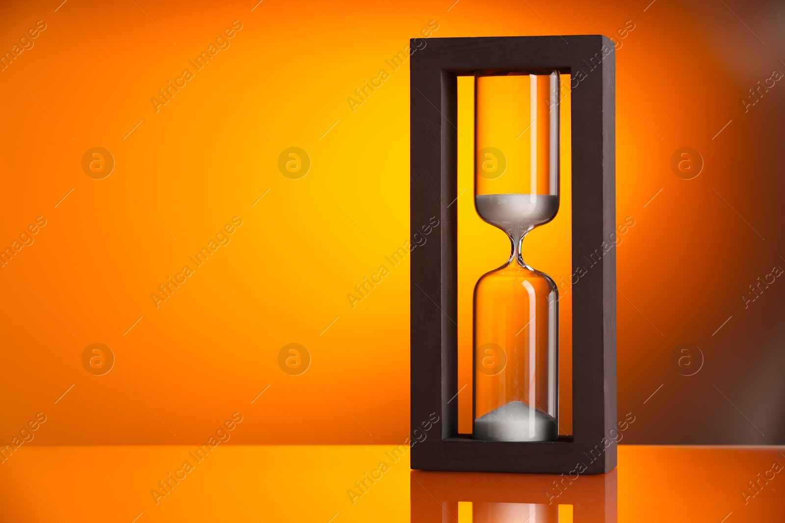 Photo of Hourglass with flowing sand on color background. Space for text