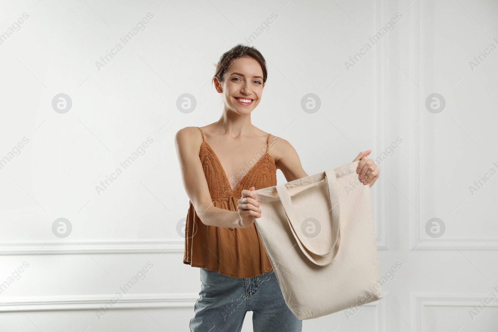Photo of Happy young woman with blank eco friendly bag near white wall