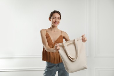 Happy young woman with blank eco friendly bag near white wall