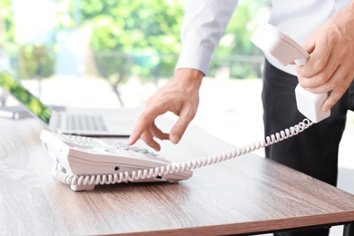 Photo of Man dialing number on telephone at workplace