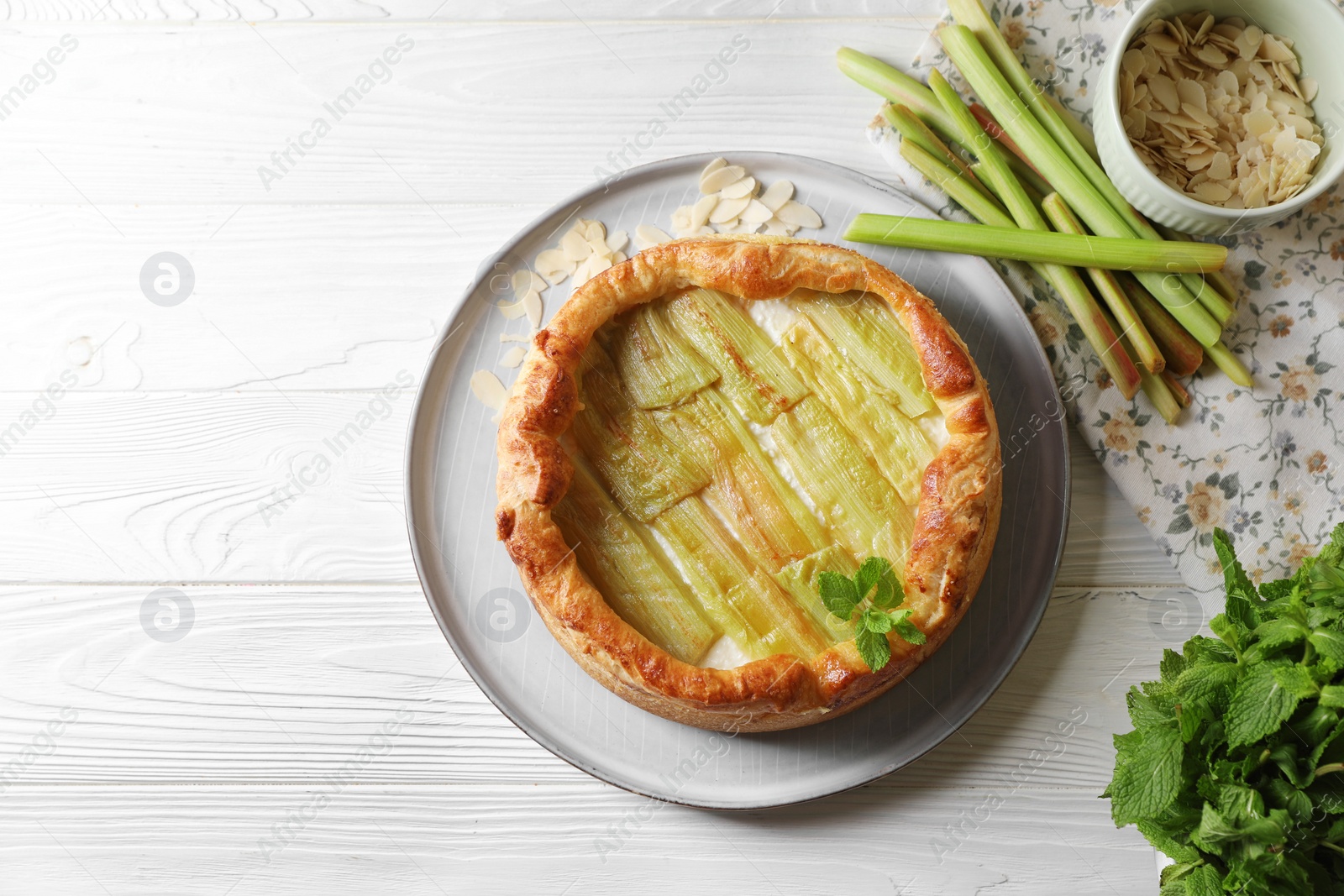 Photo of Freshly baked rhubarb pie and stalks on white wooden table, flat lay. Space for text