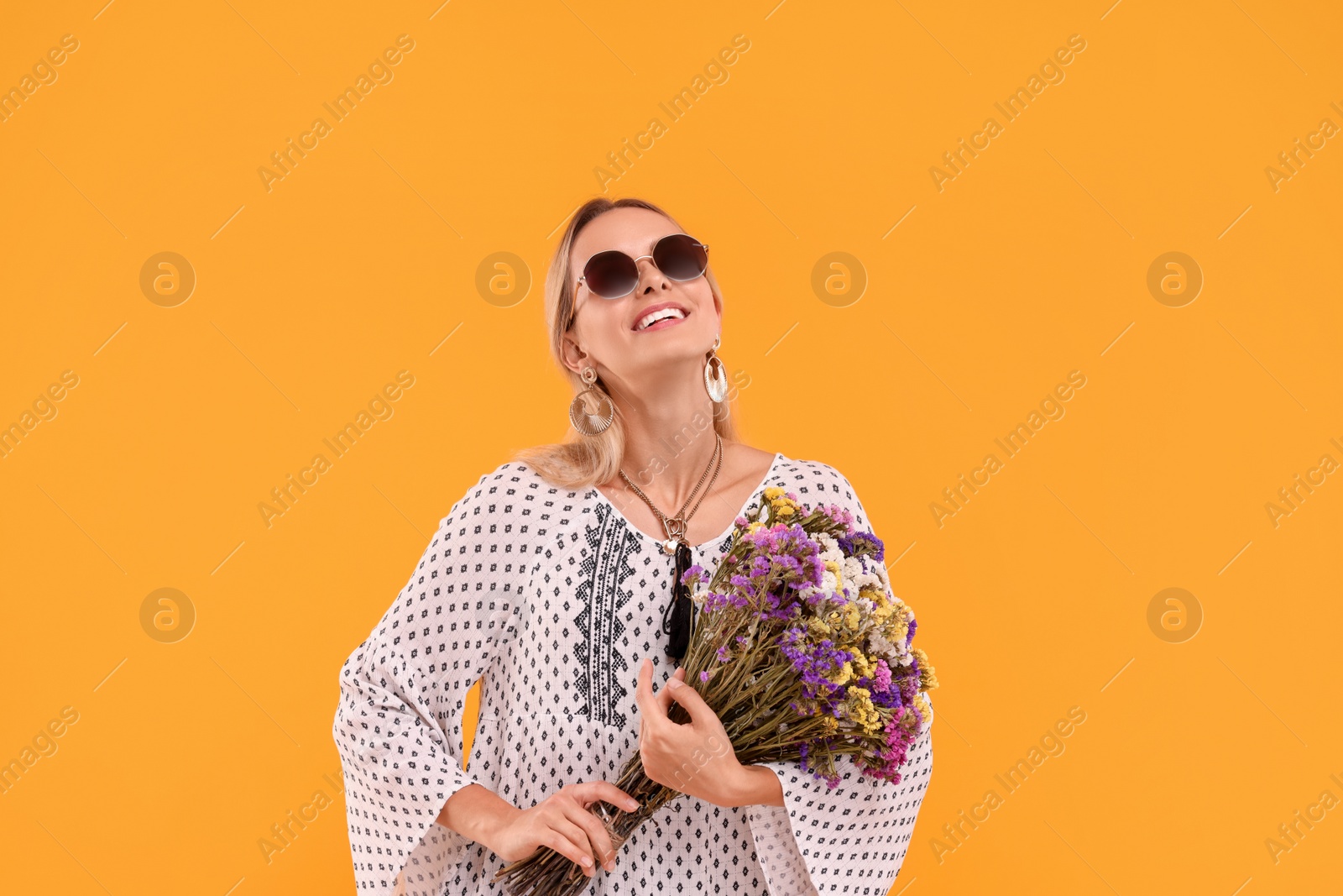 Photo of Portrait of smiling hippie woman with bouquet of flowers on yellow background