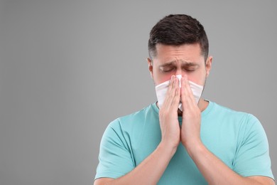 Photo of Allergy symptom. Man sneezing on light grey background. Space for text