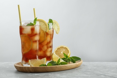 Photo of Glasses of delicious iced tea on table against light background.