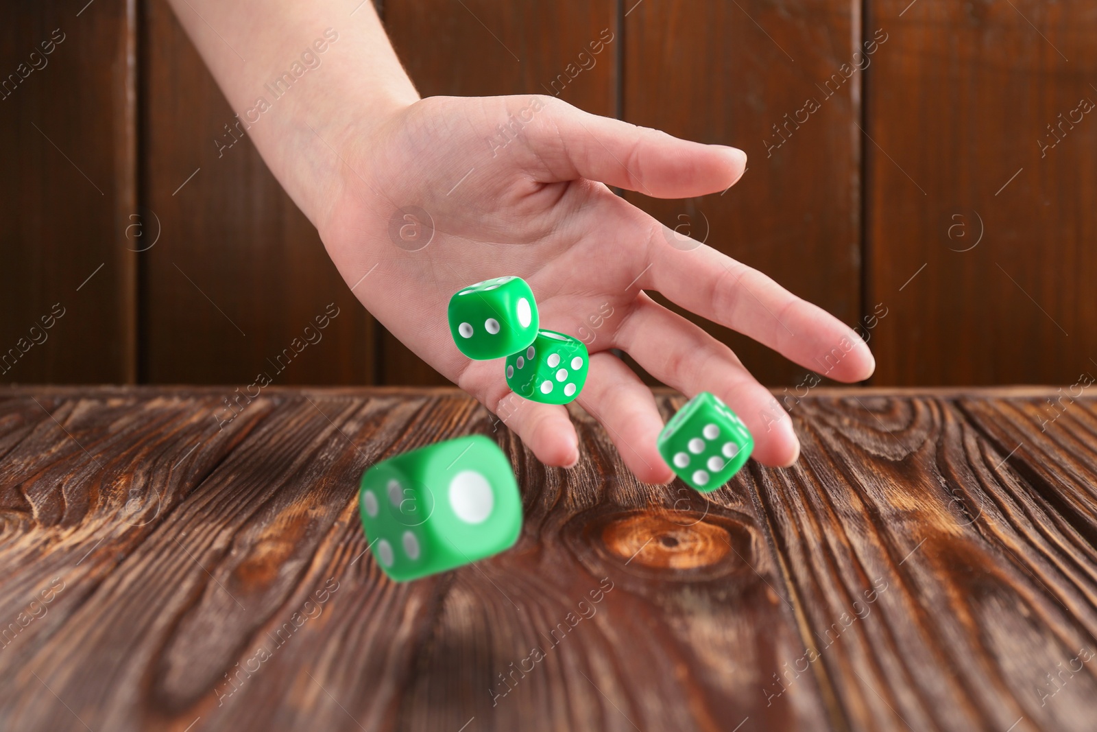 Image of Woman throwing green dice on wooden table, closeup