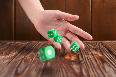 Image of Woman throwing green dice on wooden table, closeup