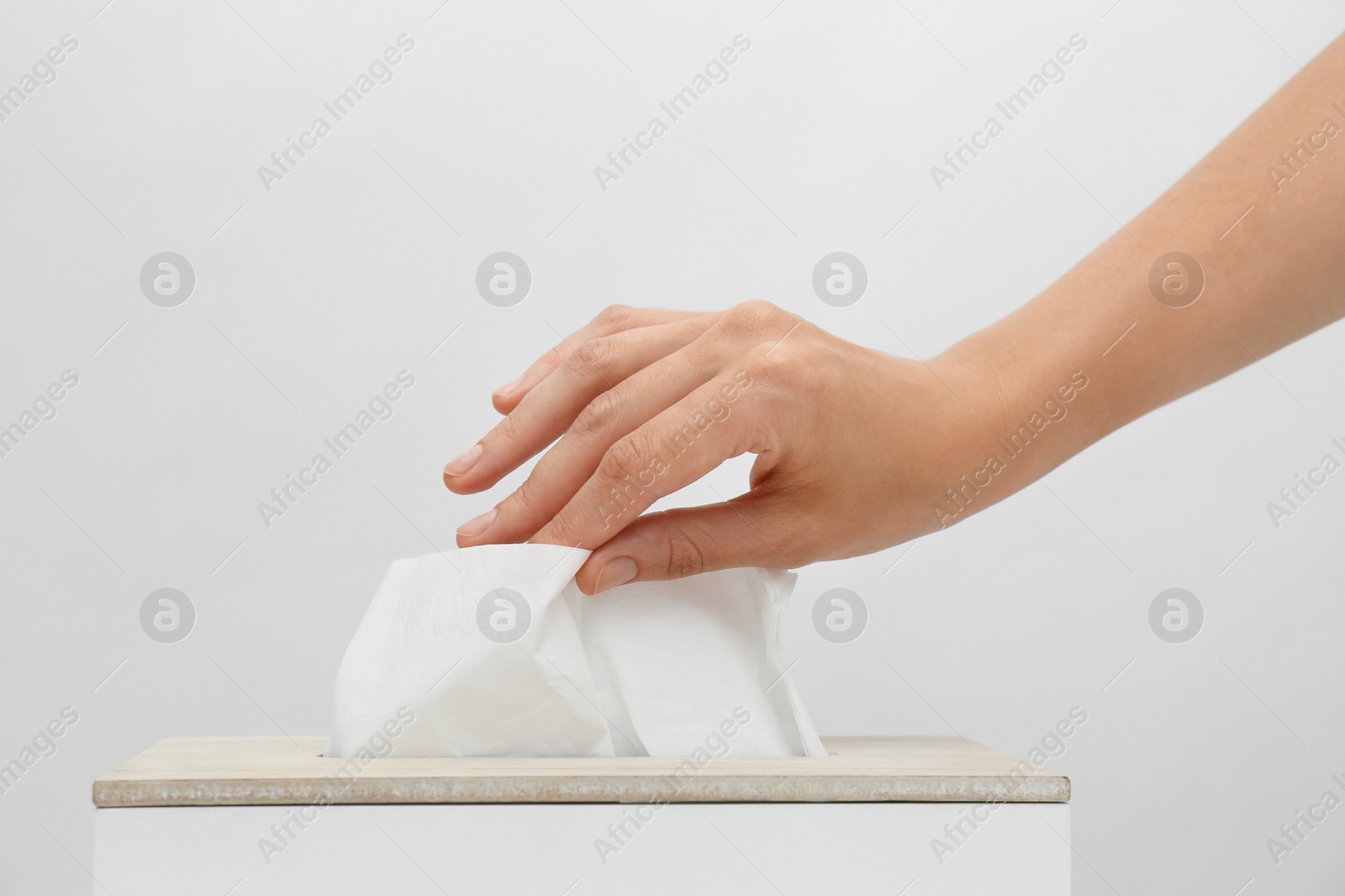 Photo of Woman taking paper tissue from holder on light background, closeup