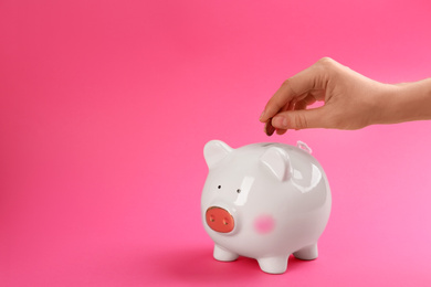 Photo of Woman putting coin into piggy bank on pink background, closeup. Space for text