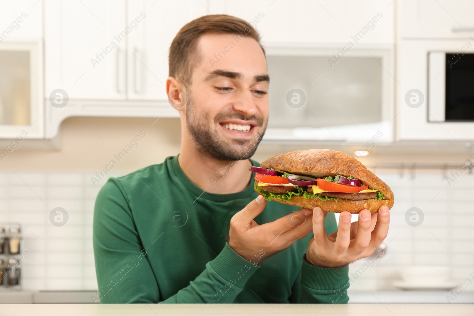 Photo of Young hungry man eating tasty sandwich in kitchen