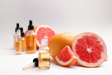 Photo of Bottles of essential oil and fresh grapefruits on white background