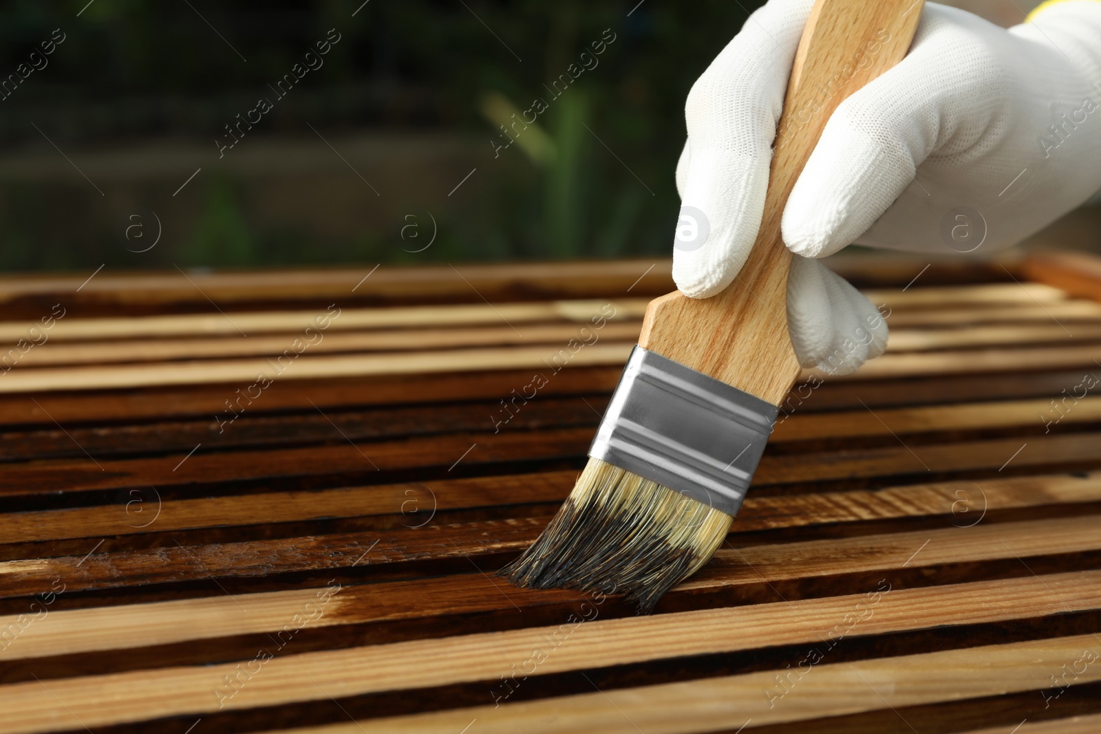 Photo of Worker applying wood stain onto planks outdoors, closeup