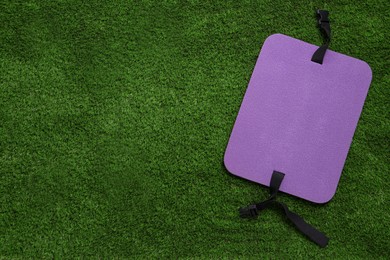 Photo of Violet foam tourist seat mat on green grass, top view. Space for text