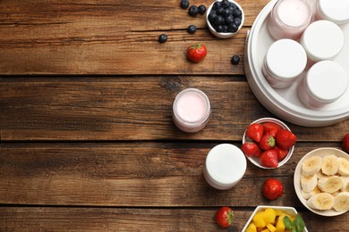 Photo of Modern yogurt maker with full jars and different fruits on wooden table, flat lay. Space for text