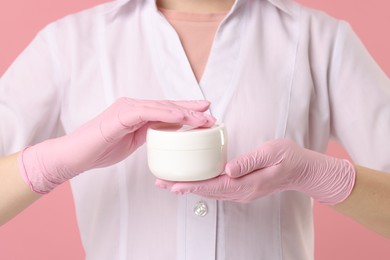Photo of Cosmetologist with cosmetic product on pink background, closeup