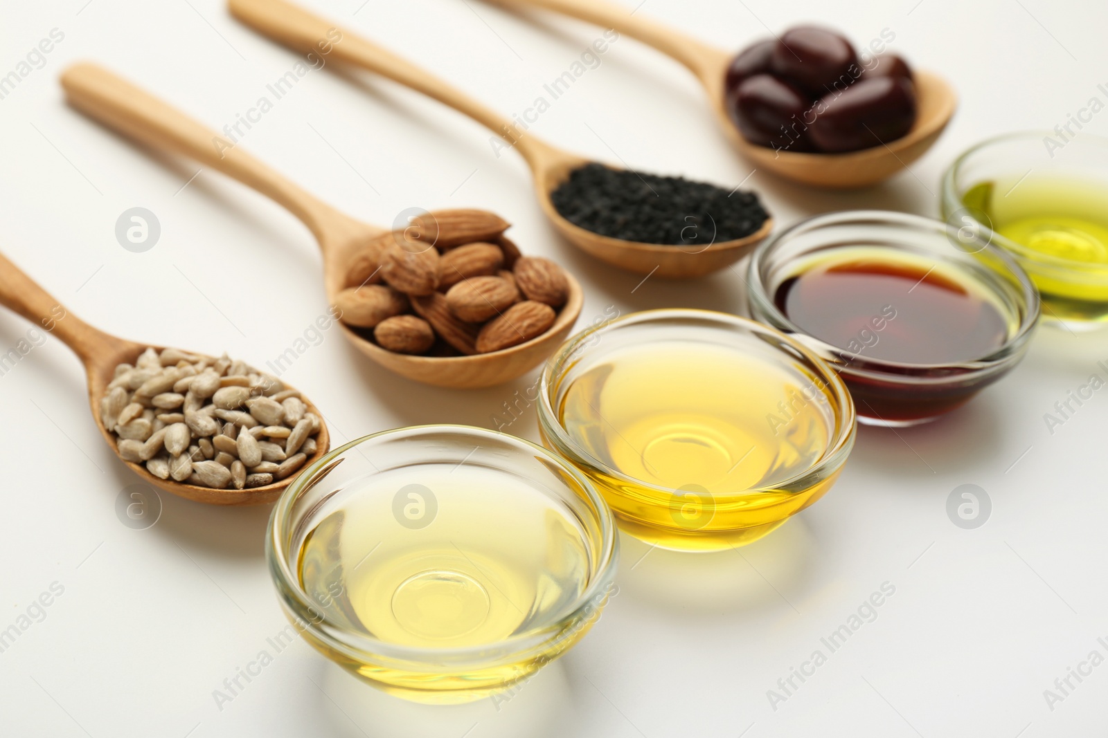 Photo of Vegetable fats. Different cooking oils in bowls and spoons with ingredients on white background, closeup