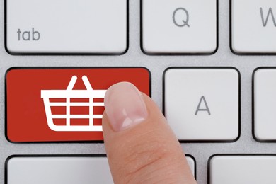 Image of Online store purchase. Woman pressing red button with shopping basket on computer keyboard, top view