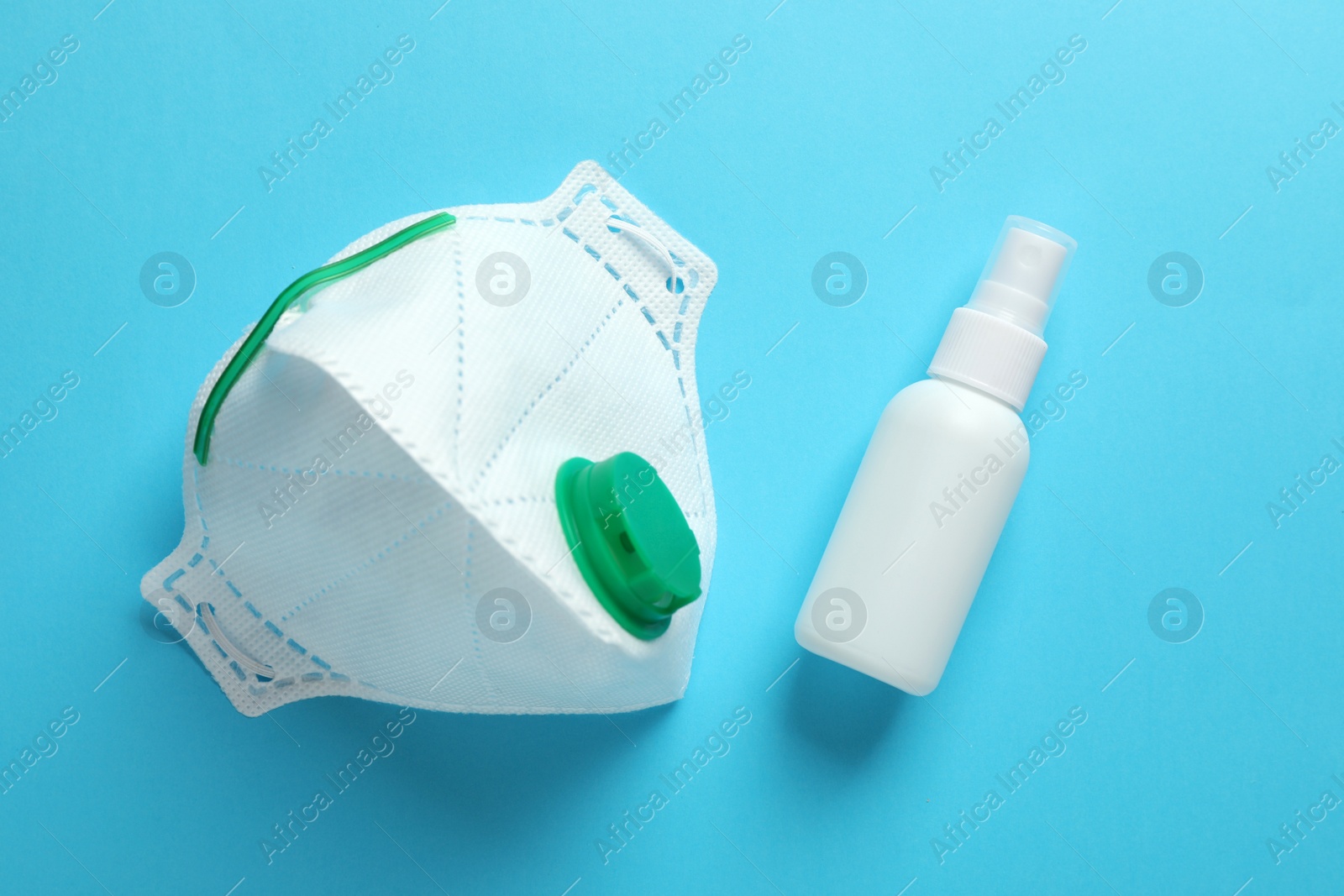 Photo of Respiratory mask and hand sanitizer on light blue background, flat lay. Safety equipment