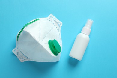 Respiratory mask and hand sanitizer on light blue background, flat lay. Safety equipment