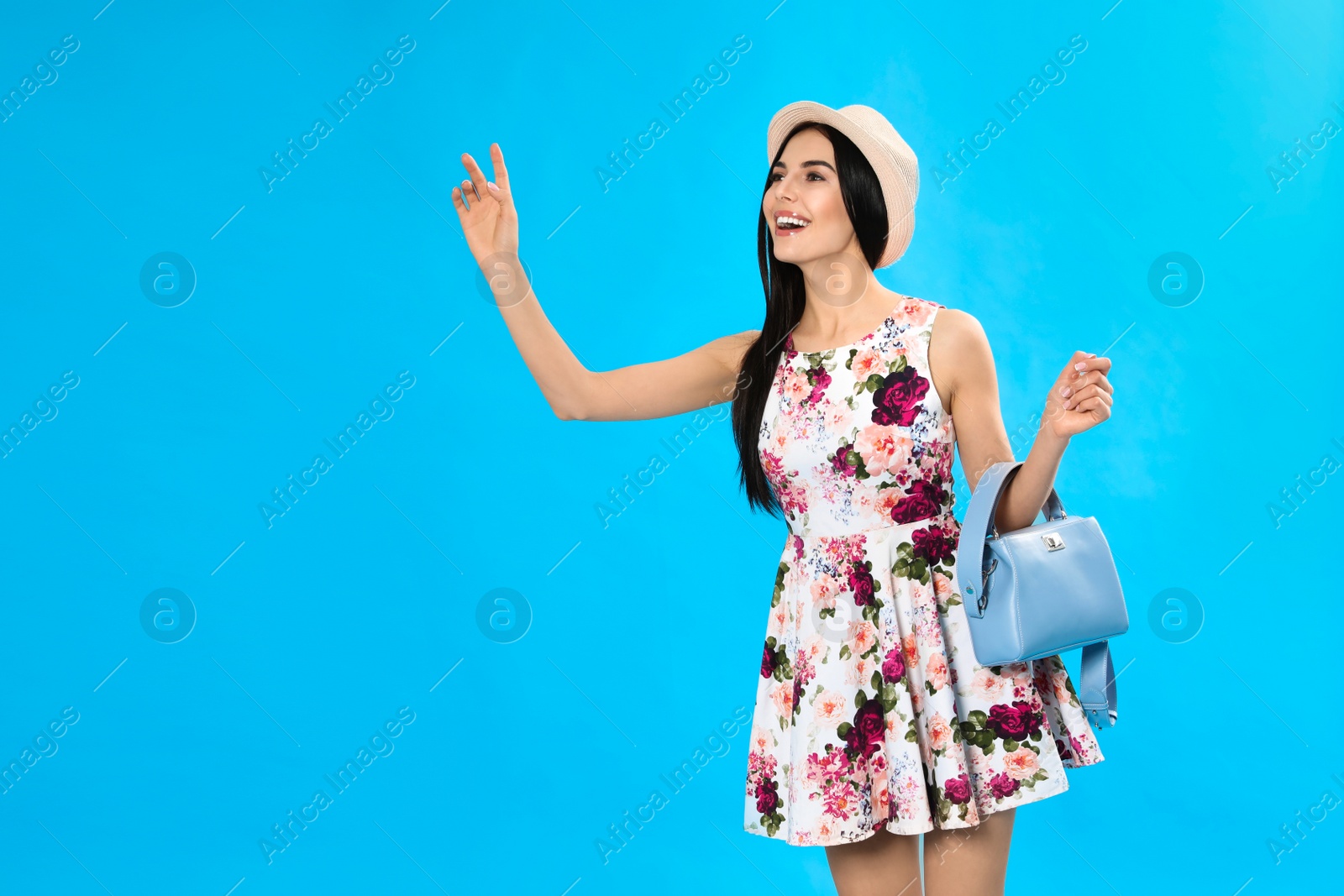Photo of Young woman wearing floral print dress with stylish handbag on light blue background