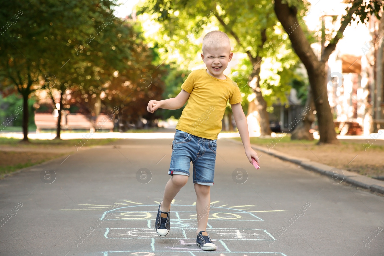 Photo of Little child playing hopscotch drawn with colorful chalk on asphalt