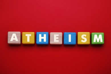 Image of Word Atheism made of wooden cubes with letters on red table, top view