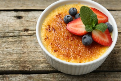 Photo of Delicious creme brulee with berries and mint in bowl on wooden table, above view. Space for text