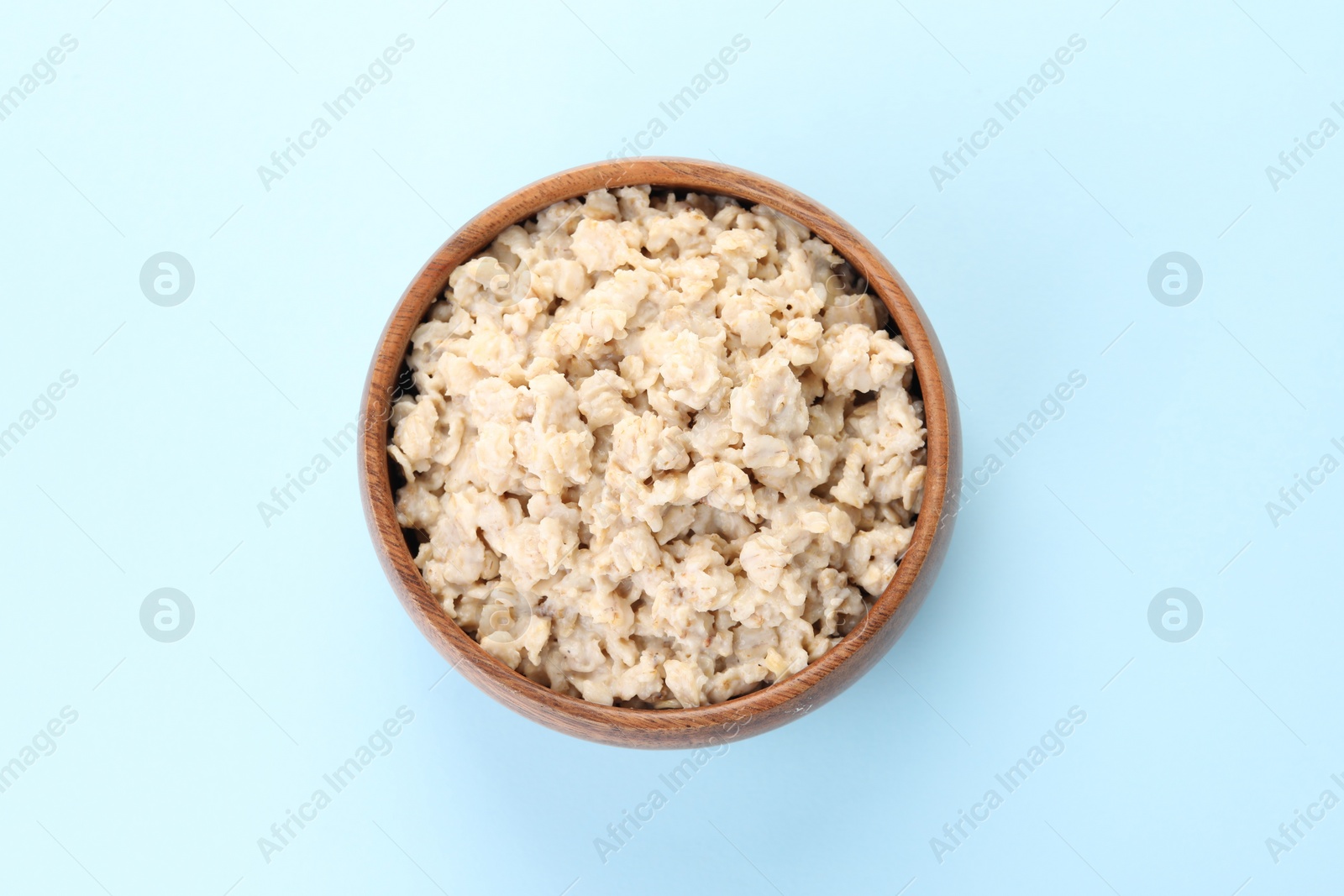 Photo of Tasty boiled oatmeal in bowl on light blue background, top view