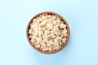 Photo of Tasty boiled oatmeal in bowl on light blue background, top view