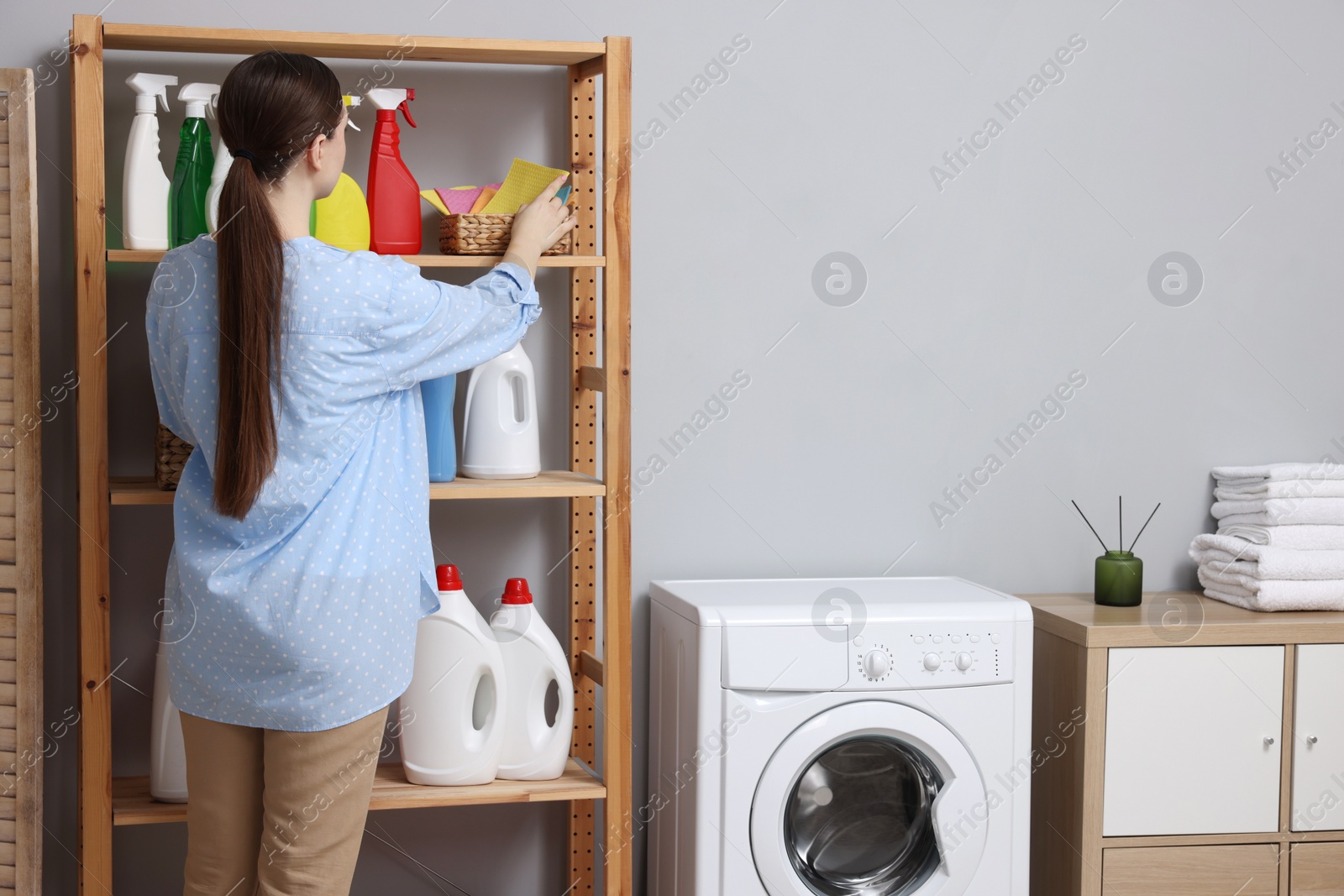 Photo of Woman taking cleaning cloth from basket in laundry room