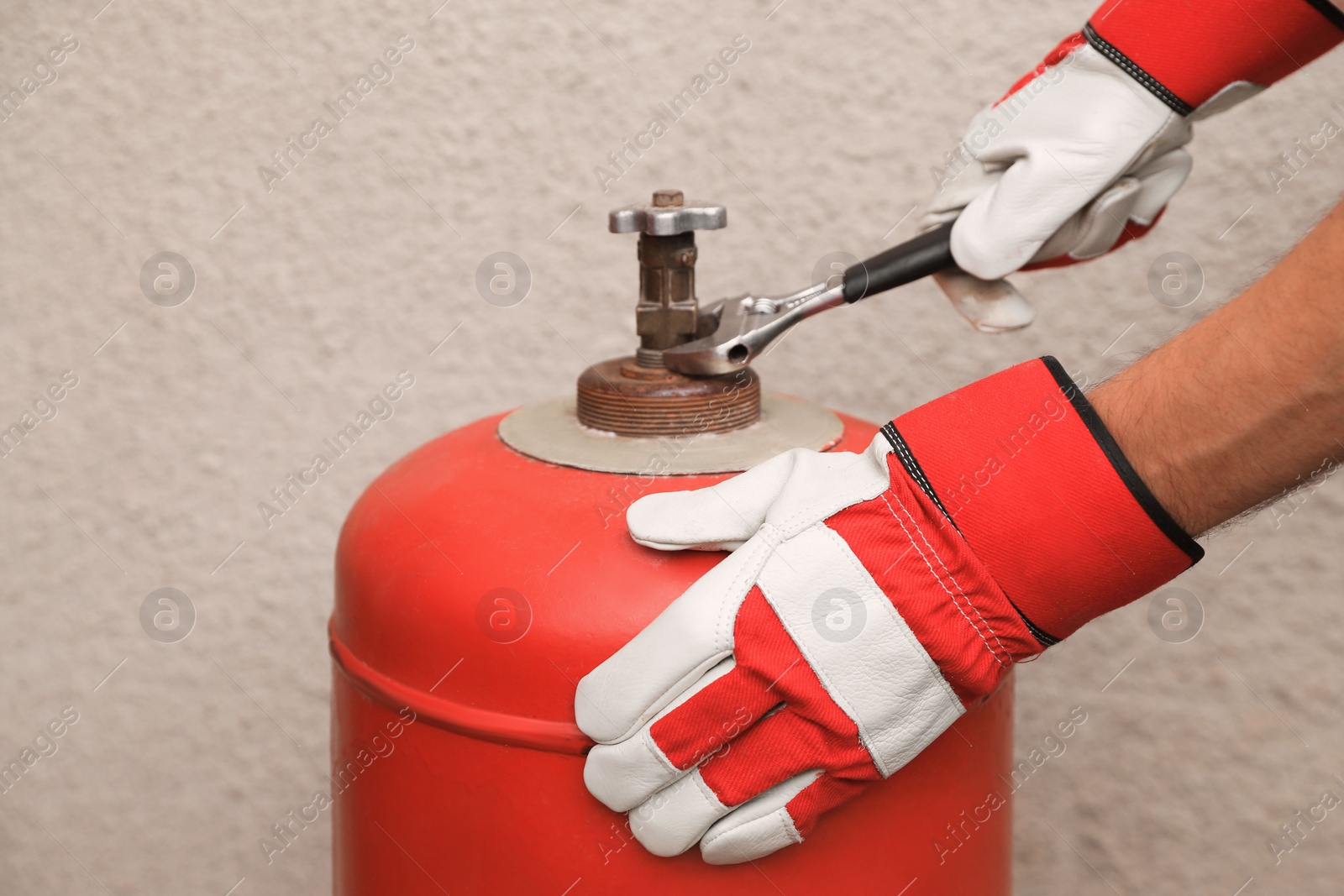 Photo of Worker with adjustable wrench opening red gas cylinder near wall, closeup