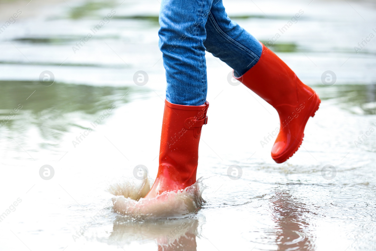 Photo of Woman with red rubber boots running in puddle, closeup. Rainy weather